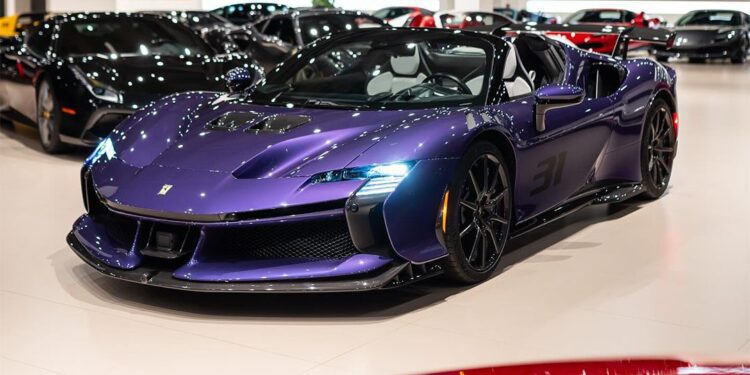 A Violetto Dino Ferrari SF90 Spider is displayed at Ferrari Lake Forest's luxury showroom, surrounded by other high-end vehicles under bright lighting.
