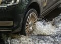 A close-up of a Range Rover wheel driving through shallow water, creating splashes around the tire.