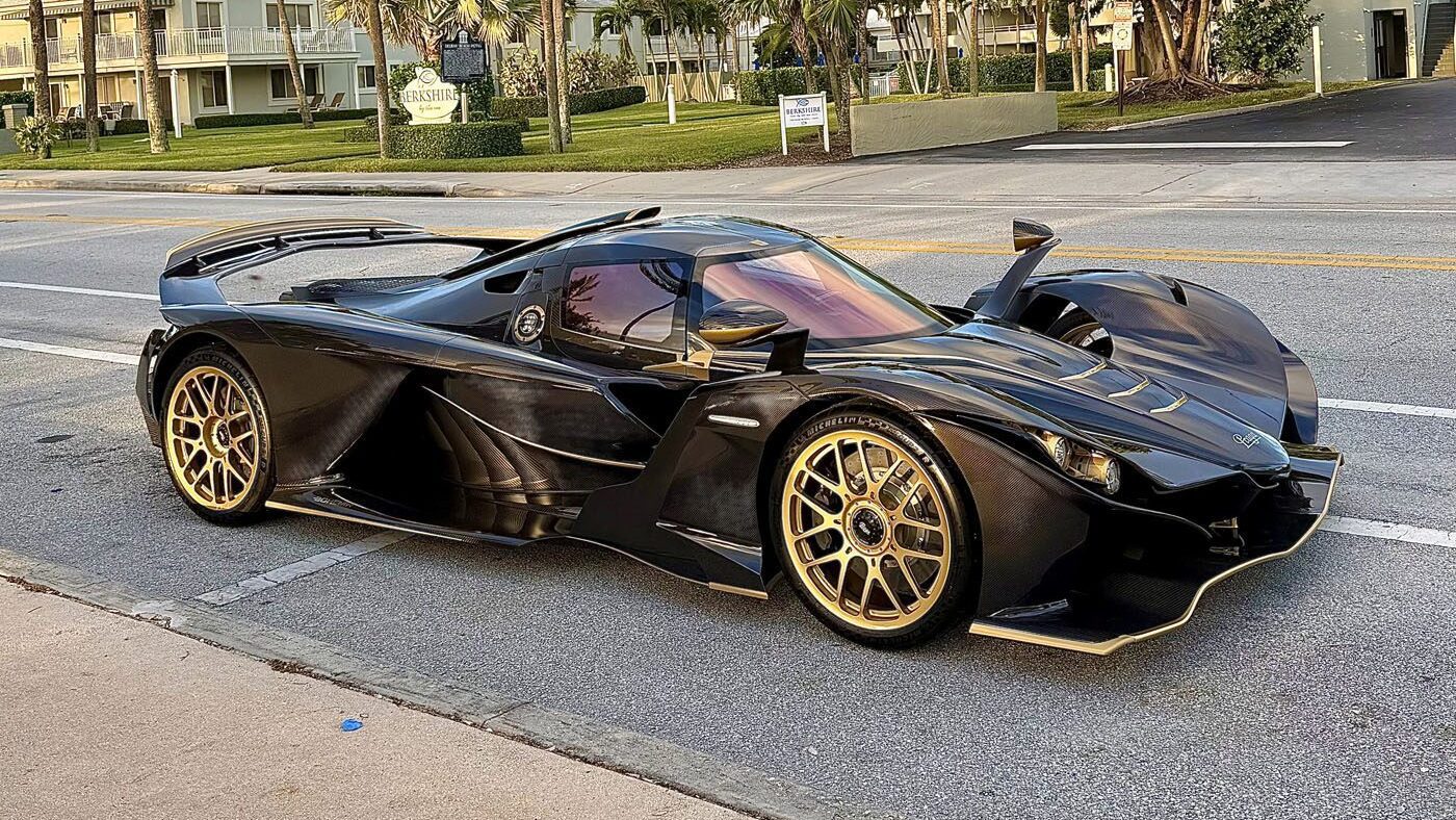 A black and gold hypercar with an aerodynamic design, reminiscent of the Praga Bohema, is parked on a street lined with palm trees and residential buildings, capturing the essence of South Florida automotive luxury.