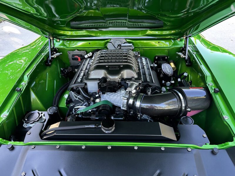 A close-up view of a car engine bay with a supercharged V8 engine, featuring a carbon fiber air intake, set in the bright green compartment of the Green Lightning 1972 AMC Javelin—a true Pro Touring masterpiece.