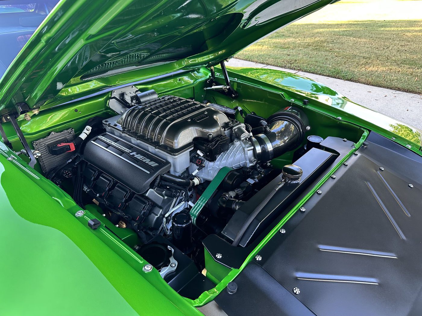 A close-up view of a high-performance Pro Touring car engine with a supercharger under the open hood of a bright green 1972 AMC Javelin.