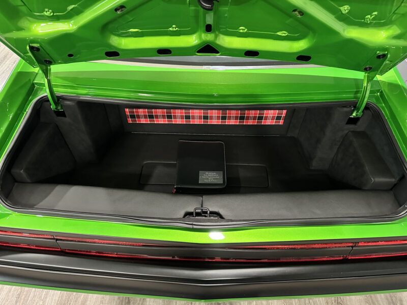 Open trunk of the Green Lightning, a bright green 1972 AMC Javelin Pro Touring, featuring a plaid-patterned panel at the back and a black rectangular item placed in the center of the trunk floor.