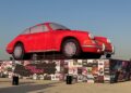 Feature Exclusive: 2025 Icons of Porsche Dubai showcases a large red inflatable car displayed on a platform decorated with various posters at this vibrant outdoor event.