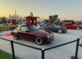 Feature Exclusive: 2025 Icons of Porsche Dubai—three classic Porsche 911 cars are displayed outdoors at an automotive event, city buildings visible in the background at sunset.
