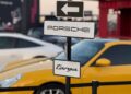 A signpost with "Porsche" and "Targa" in front of a white and a yellow Porsche car, arrow pointing left. Feature Exclusive: 2025 Icons of Porsche Dubai.