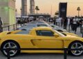 Feature Exclusive: 2025 Icons of Porsche Dubai—a row of sports cars, led by a yellow Porsche Carrera GT, is displayed at an outdoor event attended by a crowd of people.