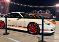 Feature Exclusive: A white Porsche GT3 RS with red wheels and detailing is displayed at an outdoor car event, surrounded by other cars and spectators, capturing the excitement of the 2025 Icons of Porsche Dubai.