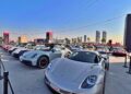 Feature Exclusive: 2025 Icons of Porsche Dubai—a row of luxury sports cars, mainly Porsches, are displayed outdoors in a city setting with tall buildings and clear skies in the background.