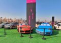 Several sports cars are displayed outdoors on green carpet, two with cartoon faces, for the Feature Exclusive: 2025 Icons of Porsche Dubai event. A tall sign reads "Classic Cars, Culture, Art," with the city skyline in the background.
