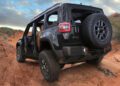 A trail-ready Jeep with no doors or roof is parked on a rugged, rocky dirt trail in a desert landscape under a cloudy sky.