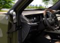 Close-up view of a modern SUV interior featuring a digital dashboard, steering wheel, and center control panel, with a park and city skyline visible through the window—inside the trail-ready 2026 Jeep Recon.
