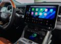 Close-up of the 2026 All-Electric Jeep Recon’s dashboard featuring a large touchscreen display with smartphone apps, steering wheel on the left, and a wireless phone charging pad below—showcasing this trail-ready SUV’s modern interior.