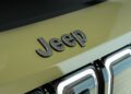 Close-up of a metallic "Jeep" logo on the hood of a green, trail-ready all-electric Jeep with part of the front grille visible.