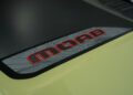 A close-up of a "MOAB" decal with red letters and topographic map design on the hood of a light green 2026 All-Electric Jeep Recon.