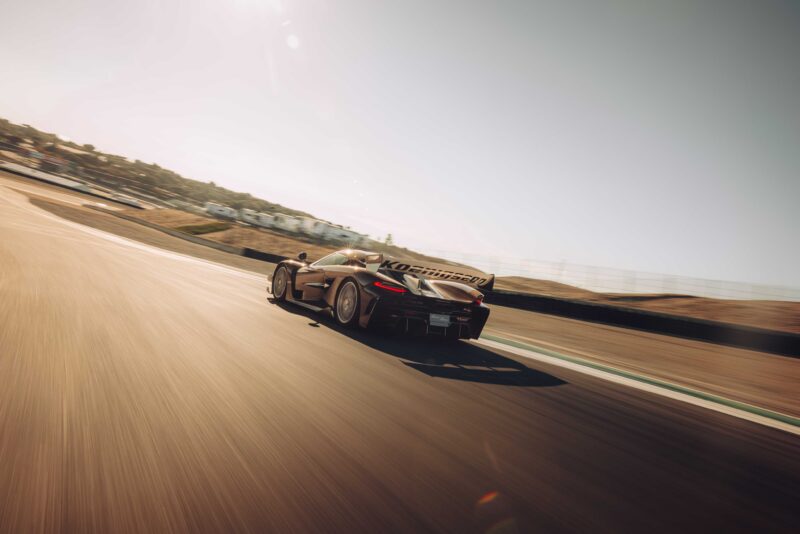 A Koenigsegg Sadair’s Spear speeds down the race track, its blurred surroundings highlighting intense motion, as distant buildings frame the moment it shatters the Laguna Seca production car record in 2025.