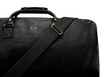 A close-up of a black leather bag with a textured surface, gold hardware, a shoulder strap, and a subtle embossed logo—perfect for those looking to upgrade your style with luxury accessories.