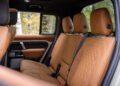 The image shows the rear passenger seats of a Defender Pickup with tan leather upholstery and diamond-pattern stitching, viewed from the open rear door—a refined touch reminiscent of Heritage Customs design.