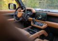 Brown leather and black steering wheel, digital dashboard, and touchscreen infotainment system inside a modern SUV, featuring tan leather trim and driver controls—crafted with Heritage Customs detail for the Defender Pickup.