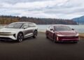 Two modern electric cars, one silver and one maroon, parked side by side on a paved area with a scenic lake, bridge, and autumn trees—reminiscent of Lucid's record Q3 deliveries amid the EV market slowdown.