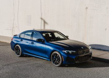 A blue BMW M340i xDrive sedan, 50 Jahre Edition, is parked on a sunlit street next to a light-colored concrete wall.