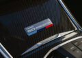 A metallic badge on a carbon fiber surface displays "3 Series 50 Jahre Edition" beside the BMW M340i’s center console with media control buttons, celebrating the xDrive legacy.