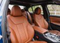 Front and rear seats of a 2026 BMW M340i xDrive with brown leather upholstery, visible dashboard controls, and trees seen through the windows.
