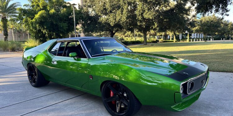 A bright green 1972 AMC Javelin muscle car is parked on a concrete driveway with trees and lawn in the background.