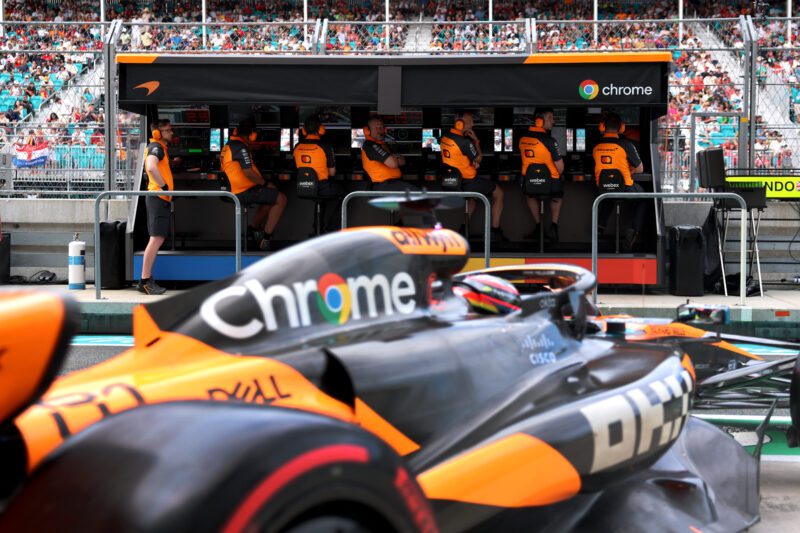 A Formula 1 race car with a Chrome logo is parked in front of engineers at a control station during a race, reminiscent of insights shared by McLaren Racing CEO Zak Brown Reveals Secrets To Success In New Autobiography.