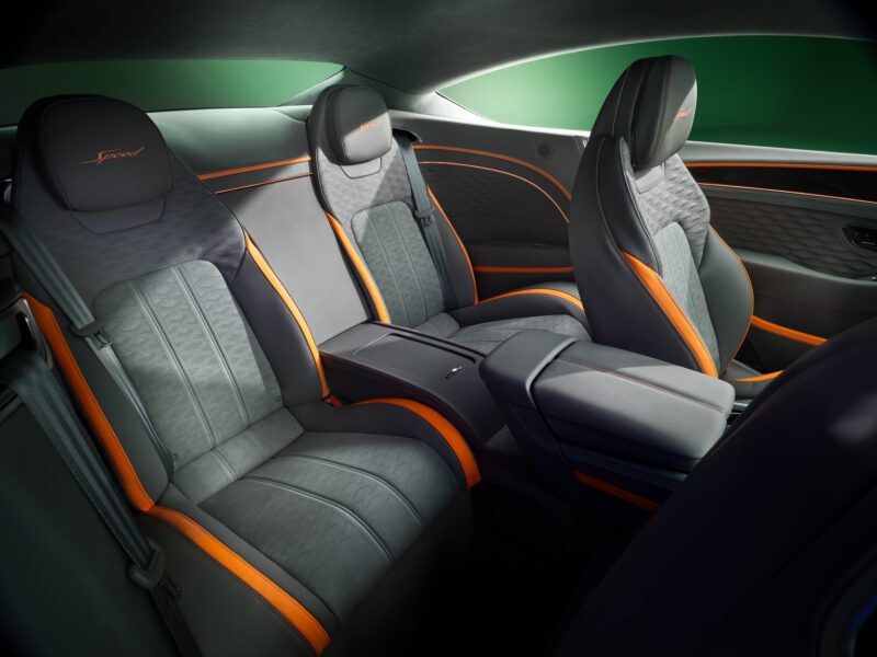 The image shows the interior of a luxury car, reminiscent of the Review: 2026 Bentley Continental GT Speed, with two rear seats, black and orange leather upholstery, and a central armrest featuring storage compartments.