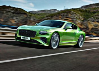 A green Bentley coupe drives on a highway with mountains and trees in the background—Review: 2026 Bentley Continental GT Speed.