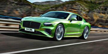 A green Bentley coupe drives on a highway with mountains and trees in the background—Review: 2026 Bentley Continental GT Speed.