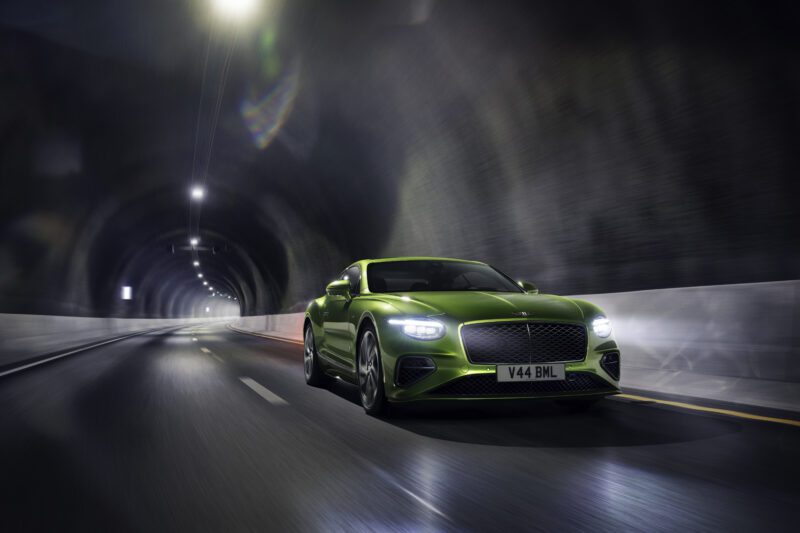 A green sports car, possibly the Review: 2026 Bentley Continental GT Speed, drives through a well-lit tunnel at speed, its headlights cutting through the darkness and blurring the road beneath its wheels.
