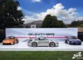 Three sports cars are displayed outdoors on a white platform in front of a "Gunther Werks" backdrop under partly cloudy skies, highlighting the latest from Gunther Werks dealers in the U.S. and Earth MotorCars.