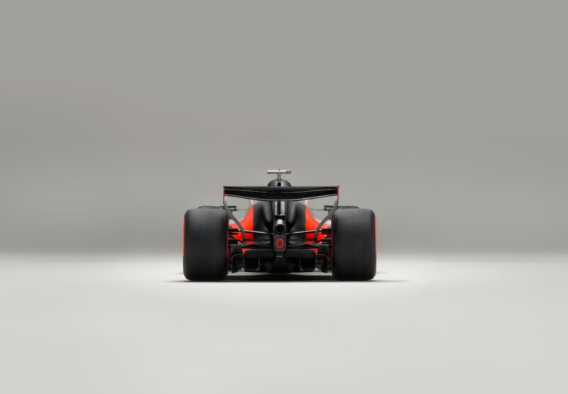 A rear view of a black and orange Audi R26 concept Formula 1 race car on a plain, light gray background.