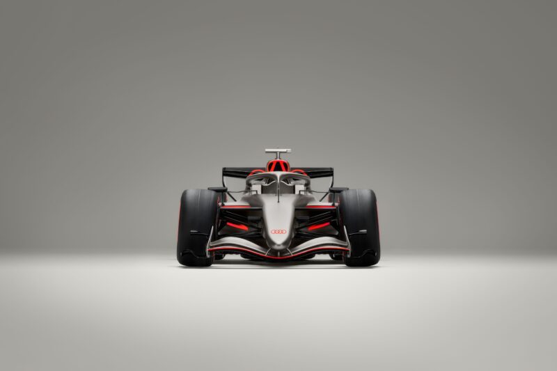 Front view of the Audi R26 concept Formula 1 race car with silver, black, and red Audi branding, showcased before its anticipated Formula 1 debut in Melbourne against a plain grey background.