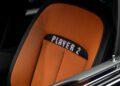 A car seat with orange upholstery displays the words "PLAYER 2" in pixelated text on the upper part of the seatback.
