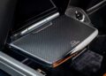 A close-up view of a fold-out tray table with a textured surface and emblem in the backseat area of a Rolls-Royce Black Badge Ghost.