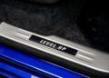A car door sill plate displays the words "LEVEL UP" in illuminated text against a metallic and blue trim, with black carpet visible—bringing a Gamer-inspired touch to the luxurious aura of a Rolls-Royce Black Badge Ghost.