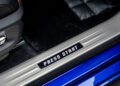 Close-up of a car door sill with a digital-style "PRESS START" sign in pixelated letters, evoking gamer vibes, next to a black carpeted floor and the striking blue exterior of a Rolls-Royce.