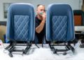 A man works on two blue, diamond-stitched car seats at a workshop table, focusing on upholstery details for the Morgan Plus Four 75th Anniversary edition.