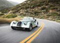 A classic mint green Morgan Plus Four convertible car drives along a winding mountain road lined with vegetation, celebrating the 75th Anniversary of this iconic model in the US.