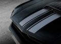 Close-up of a black muscle car hood with matte black racing stripes and a prominent hood scoop, parked on concrete—evoking the bold style of Ringbrothers’ 800-plus horsepower 1969 Ford Mustang Mach 1 ‘KINGPIN’ unveiled at the 2025 SEMA show.