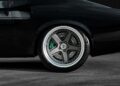 Close-up of the rear wheel of a black car, featuring a large alloy rim and a visible green Brembo brake caliper, inspired by the Ringbrothers Unveils 800-Plus Horsepower 1969 Ford Mustang Mach 1 'KINGPIN' at 2025 SEMA.