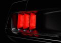 Close-up of the rear tail light of a car, illuminated red, with three vertical light bars—evoking the bold design seen on the Ringbrothers Unveils 800-Plus Horsepower 1969 Ford Mustang Mach 1 'KINGPIN' at 2025 SEMA—set against a dark background.