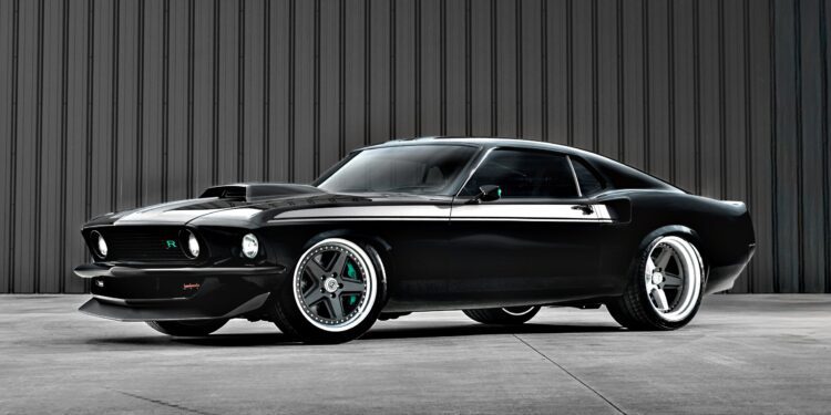 A black classic Ford Mustang with custom modifications, reminiscent of the Ringbrothers' 800-plus horsepower 1969 Mach 1 'KINGPIN' unveiled at the 2025 SEMA, is parked in front of a gray corrugated metal wall.