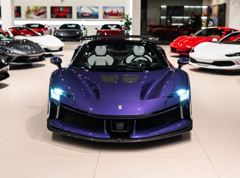 A Violetto Dino Ferrari SF90 XX Spider is displayed at Ferrari Lake Forest’s showroom, with other high-end cars visible in the background.