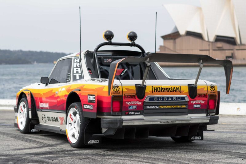 A modified Subaru Brataroo race truck with a large rear wing and colorful decals is parked by the water, with the Sydney Opera House in the background—a true Gymkhana-inspired build ready for SEMA 2025.