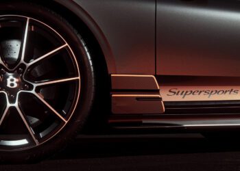 Close-up of a black luxury sports car’s front wheel and side panel with the word "Supersports" and bronze accents visible in low lighting.