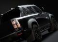 A black modern Defender Pickup is shown from a low rear angle against a dark background, highlighting its tail lights and rugged design features.