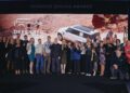 A large group of people pose for a photo on stage in front of a Defender Service Awards sign and an image of a white SUV in a desert landscape.